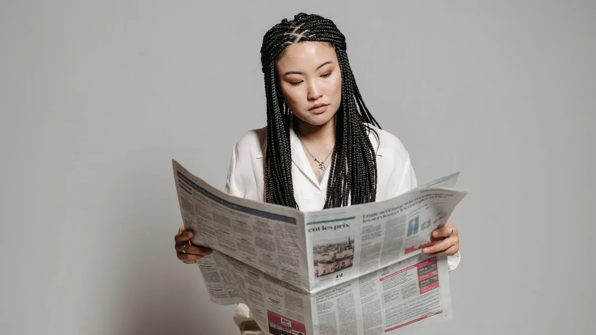 Woman with braided hairstyle reading a newspaper indoors