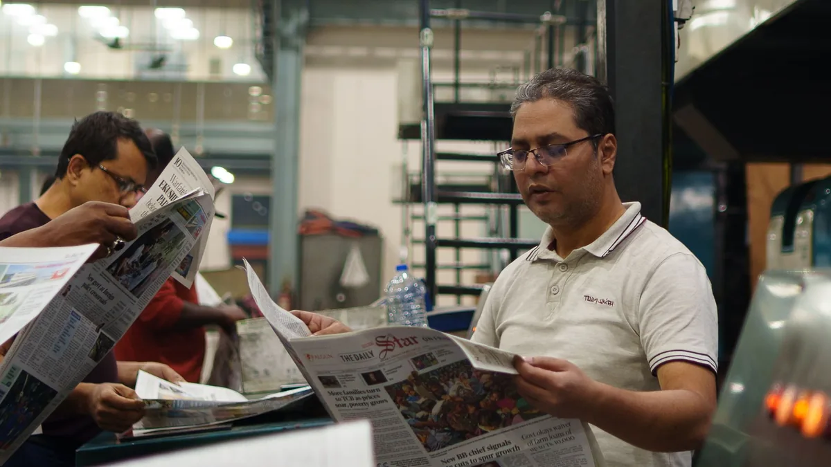 Workers at a newspaper printing press reading freshly pr