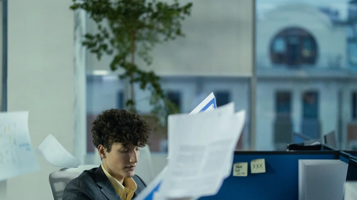 Young man in office cubicle tossing papers illustrating