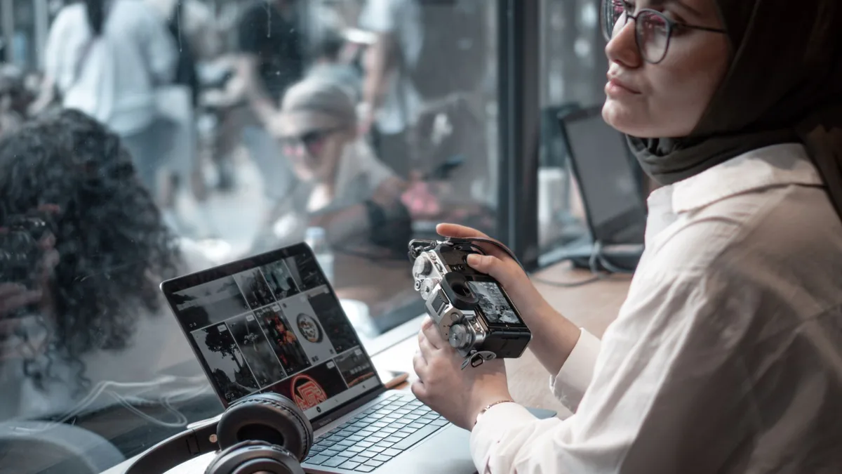 Young woman in hijab using laptop and camera in a cozy c