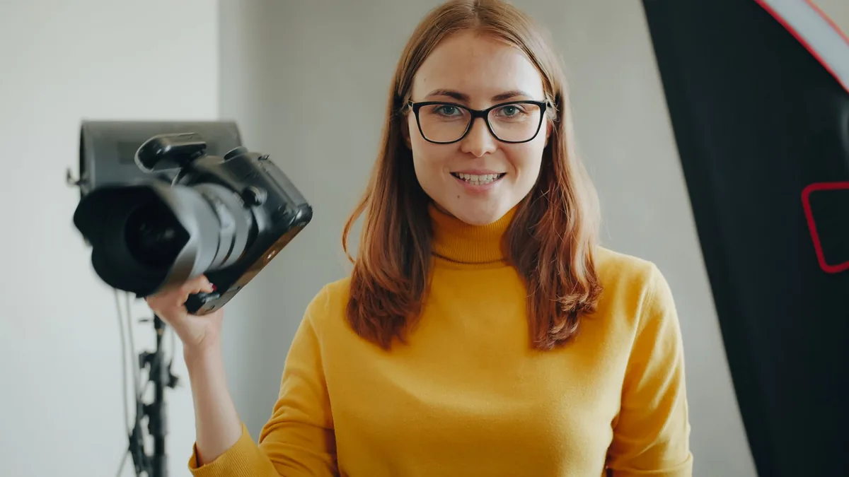 Young woman photographer smiling with camera in professi